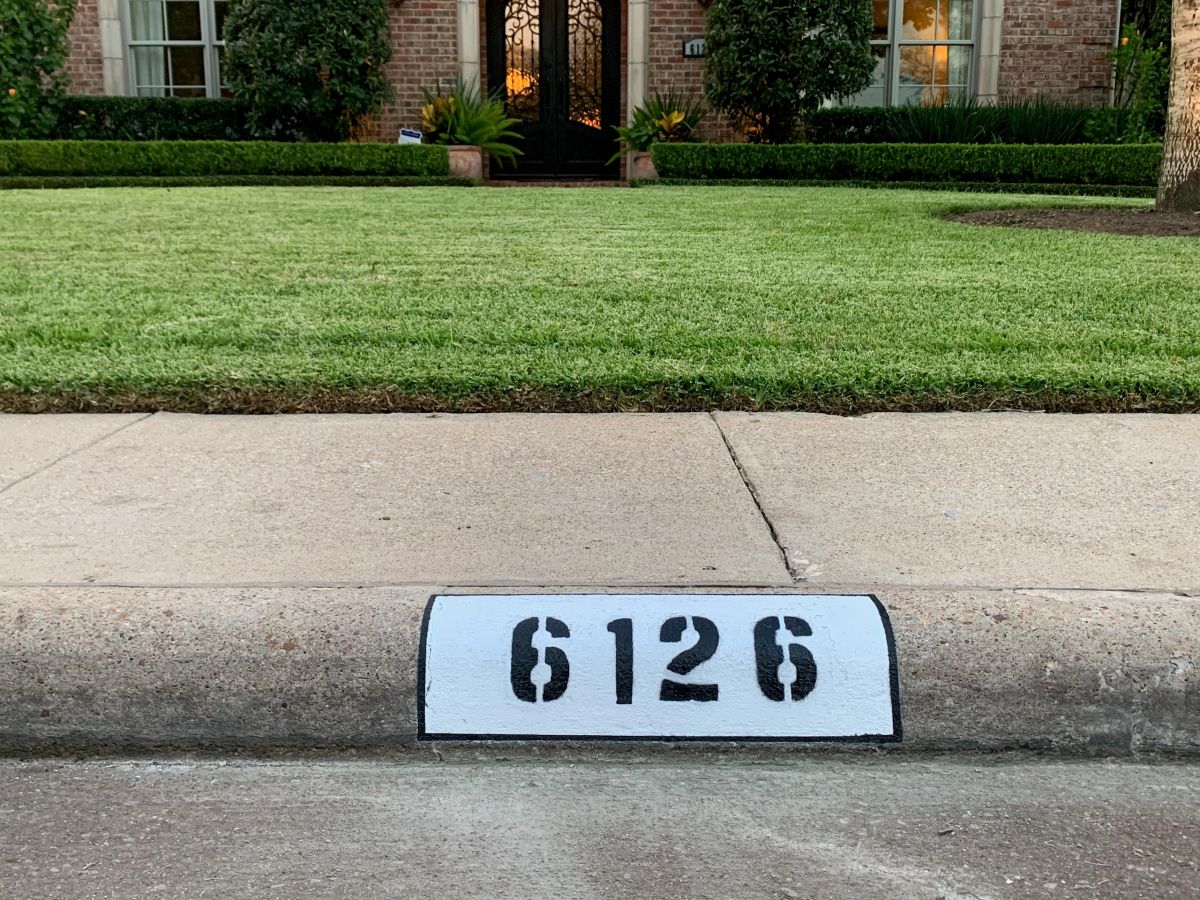 City Curb Painting’s black address numbers painted on a white curb in front of a Houston-area home